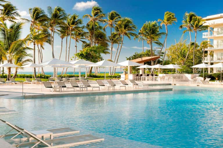 Luxury beachfront pool with white umbrellas, palm trees, and ocean view at resort
