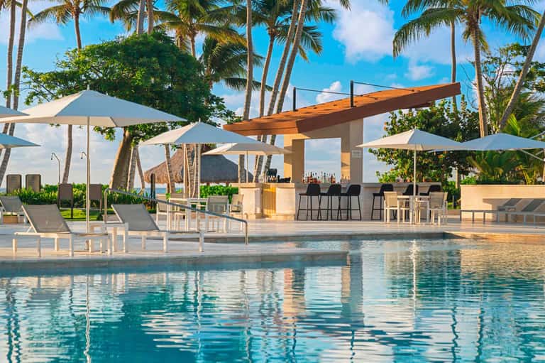 Luxury beachfront resort pool with umbrellas, bar, palm trees, and ocean view
