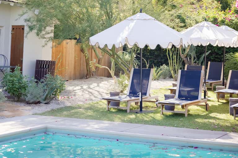 Garden pool area with white umbrellas, navy lounge chairs, and lush green landscaping