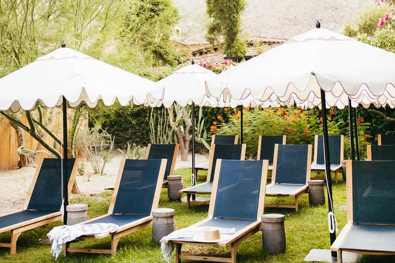 Outdoor lounge area with navy chaise lounges under white umbrellas and lush vegetation