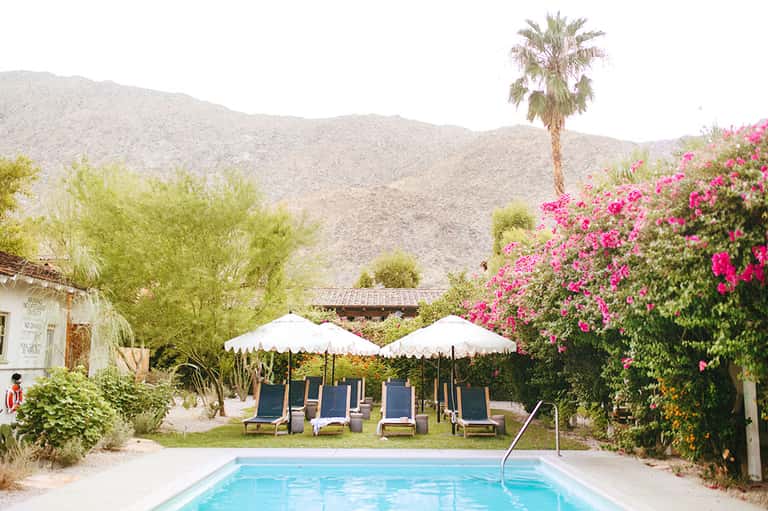 Desert resort pool surrounded by mountains, vibrant pink bougainvillea, and white umbrellas