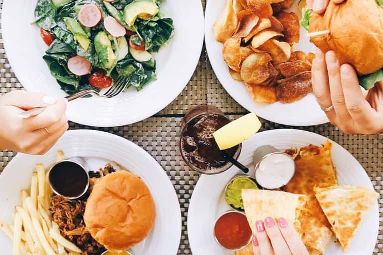 Overhead view of meals including salad, sandwich with fries, quesadilla, and chocolate sauce on white plates