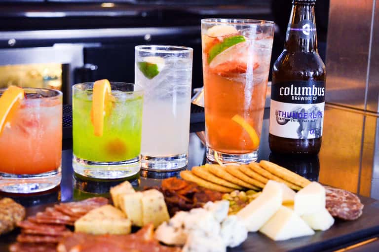 Colorful cocktails and craft beer with charcuterie board on dark counter