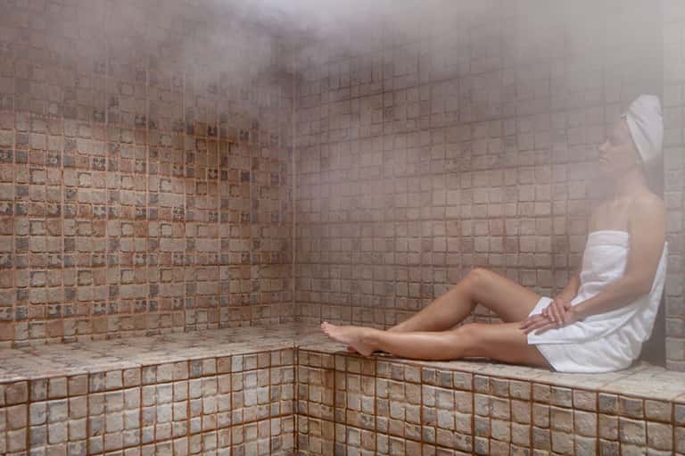 Woman relaxing in a steamy spa room with terracotta tile walls and heated bench seating