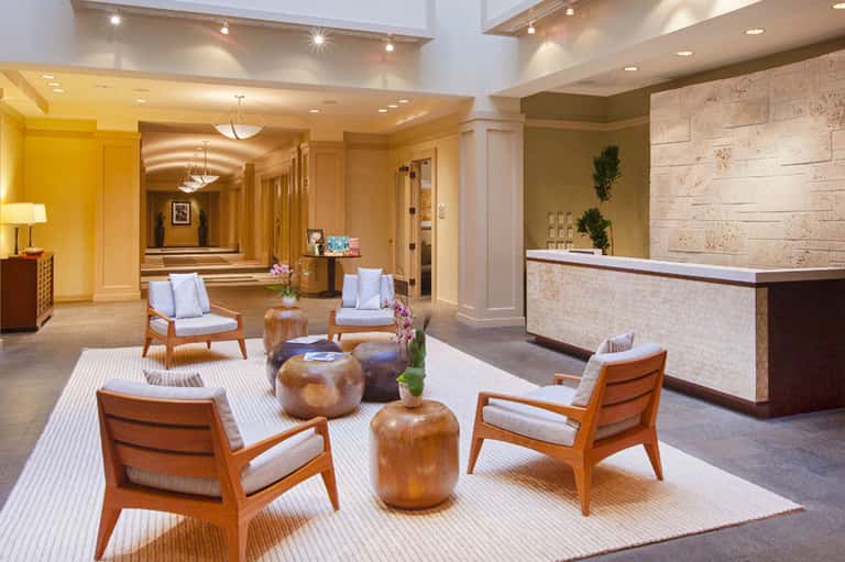 Modern hotel lobby with wooden mid-century chairs, travertine reception desk, and ambient lighting