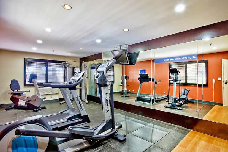 Modern fitness center with exercise equipment, mirrored walls, and orange accent walls