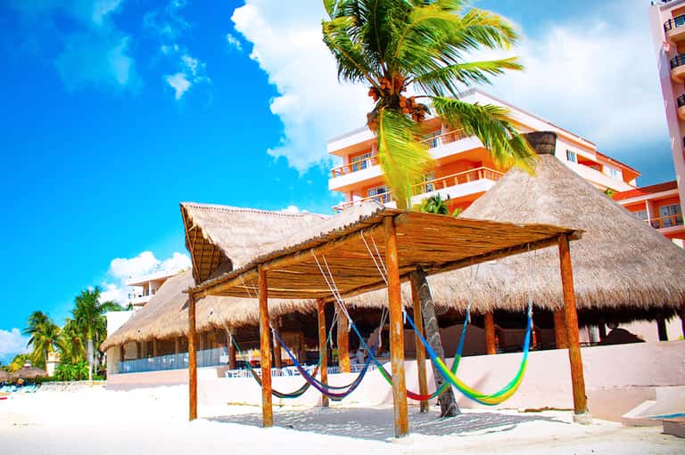 Beachfront resort pool with hammocks, thatched structures, and tropical palms