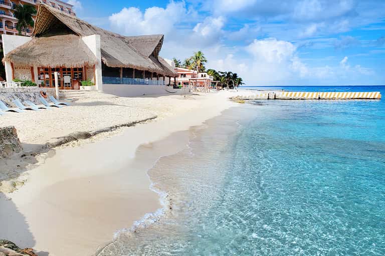 Tropical beach resort with thatched-roof bungalows, white sand, and crystal-clear turquoise water