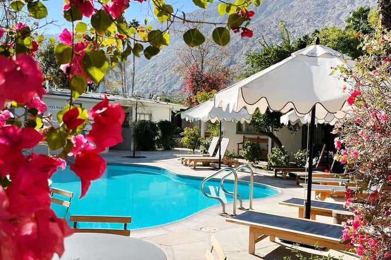 Resort pool surrounded by magenta bougainvillea flowers, white umbrellas, and mountain views