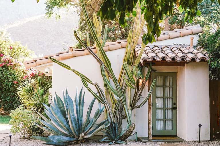 White stucco cottage with terracotta roof and blue agave plants in landscaped garden