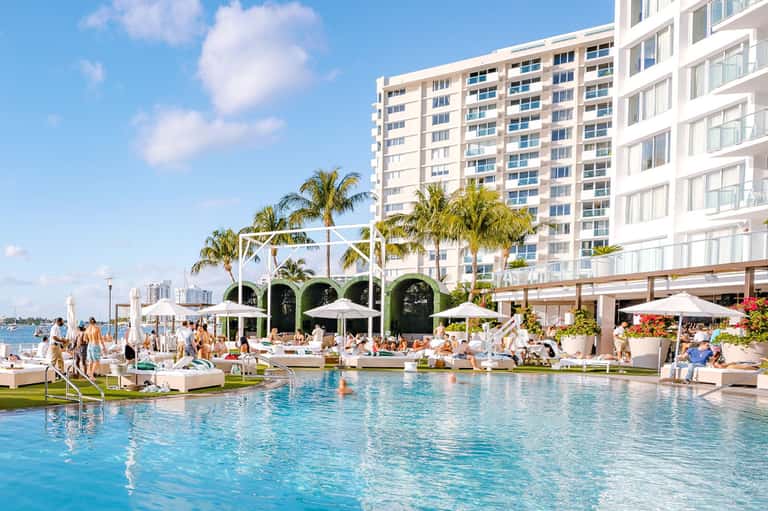 Luxury resort pool with lounge chairs, white cabanas, and waterfront high-rise building