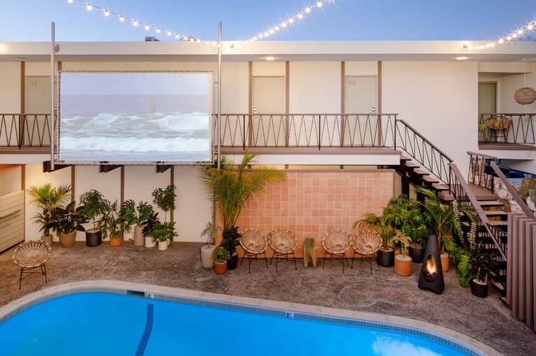 Beachfront pool deck with blue lounge chairs, palm trees, and ocean view with string lights overhead