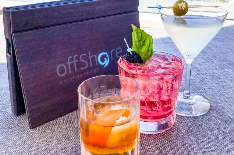 Offshore lounge cocktail menu with three colorful drinks and purple branded menu card on table