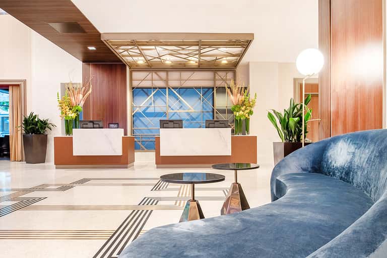 Contemporary hotel lobby with dual reception desks, marble floors, and geometric window design