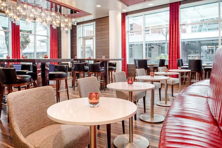 Modern lounge area with round white tables, upholstered chairs, red curtains, and floor-to-ceiling windows