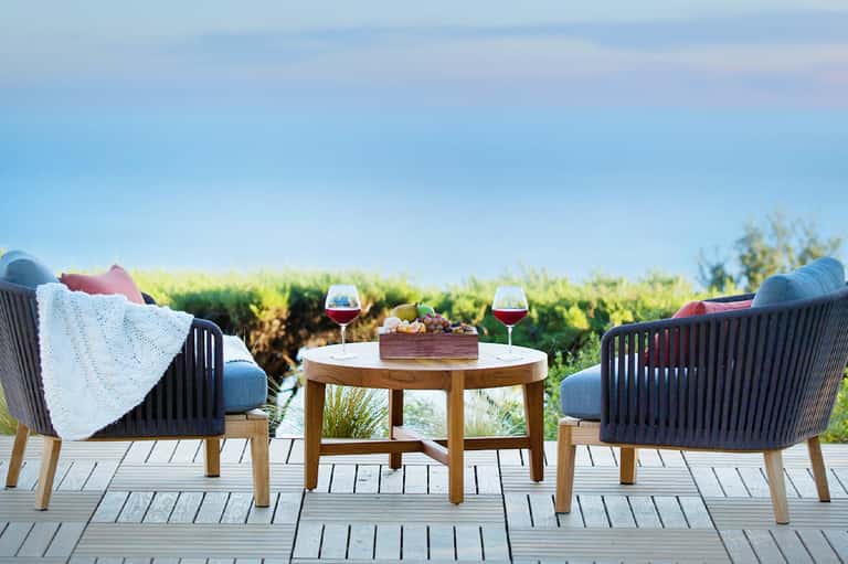 Two lounge chairs facing a wetland landscape with wine glasses and blanket on a wooden deck