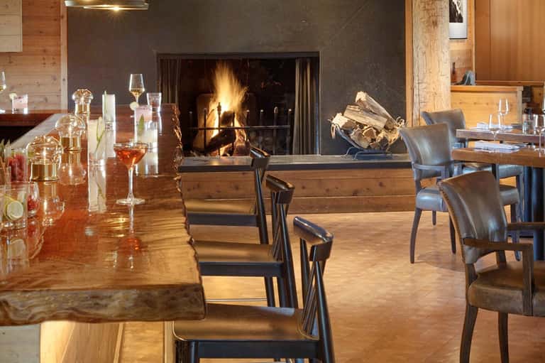 Modern fireplace lounge with wooden bar counter, leather chairs, and elegant glassware display