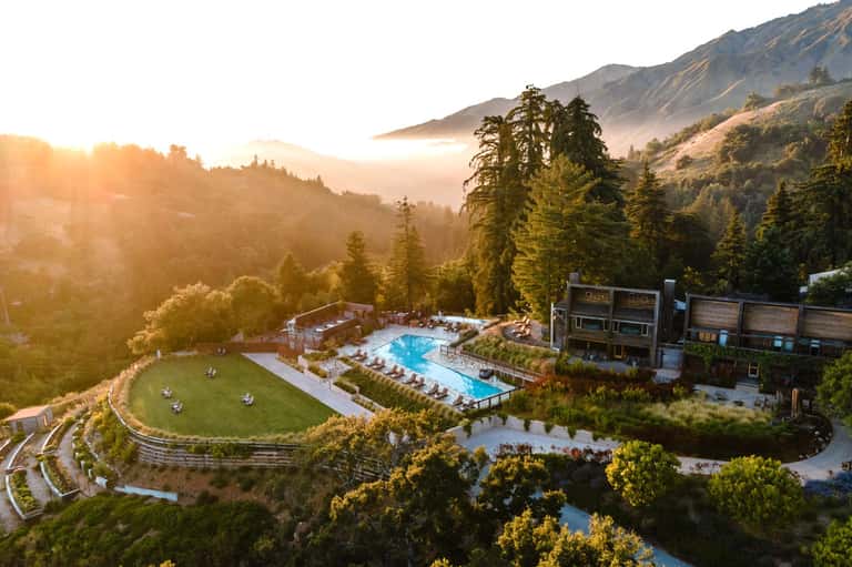 Mountain resort with large swimming pool, lawn seating area, and forest landscape at golden hour