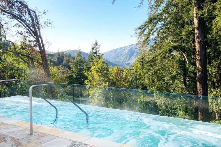 Infinity pool with glass railing overlooking forested mountain valley landscape