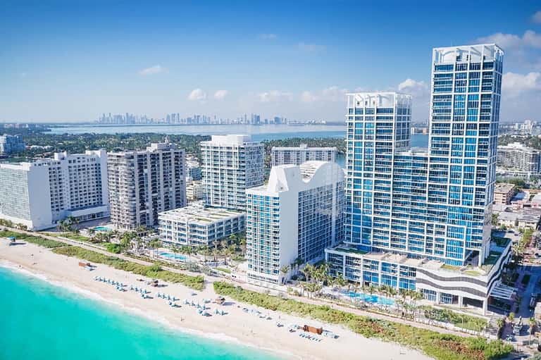 Aerial view of beachfront high-rise hotels with turquoise ocean, white sand beach, and city skyline in background