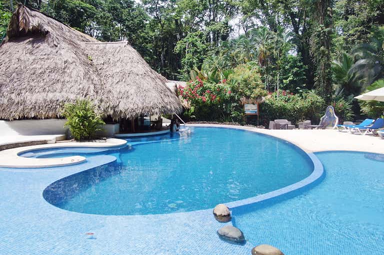 Resort pool with thatched-roof cabana, lush jungle vegetation, and lounge chairs