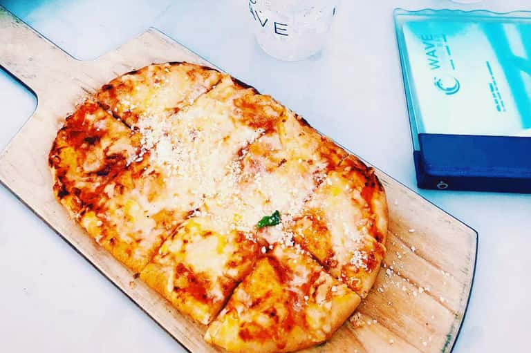 Freshly baked pizza with cheese on wooden board by poolside