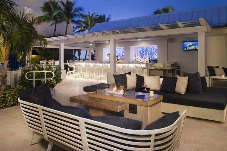 Beachfront resort lounge at dusk with fire pit, striped outdoor seating, ocean and palm tree views