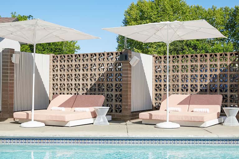 Poolside daybeds with white umbrellas and decorative brick privacy screens