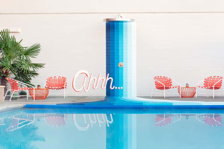Pool area with blue water feature, red chairs, and palm tree backdrop