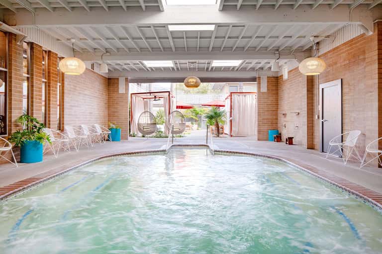 Indoor swimming pool with lane markers in brick-walled facility with pendant lighting and lounge chairs