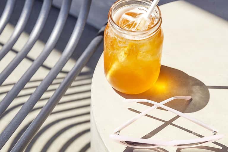 Glass of iced tea with straw on white table with striped shadow