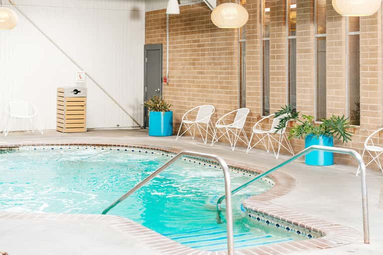 Indoor pool with spa jets, white modern chairs, and brick architecture