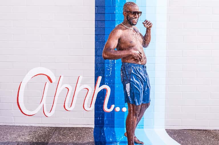 Mural art of man in swim shorts with text reading 'Ohhh...' on white and blue tiled wall