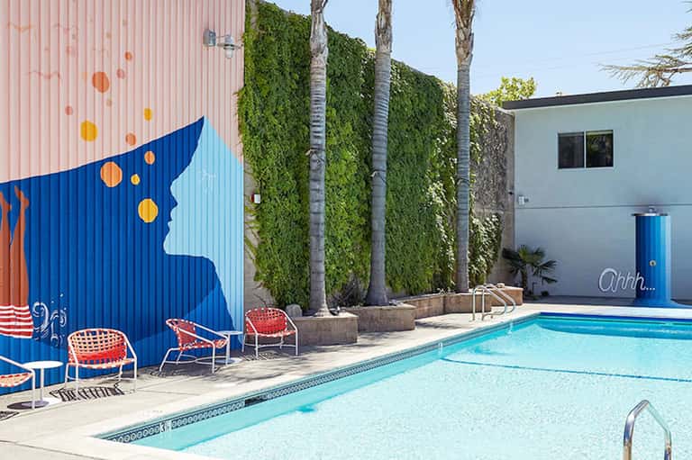 Modern pool area with blue mural art wall, ivy-covered pillars, and colorful lounge chairs