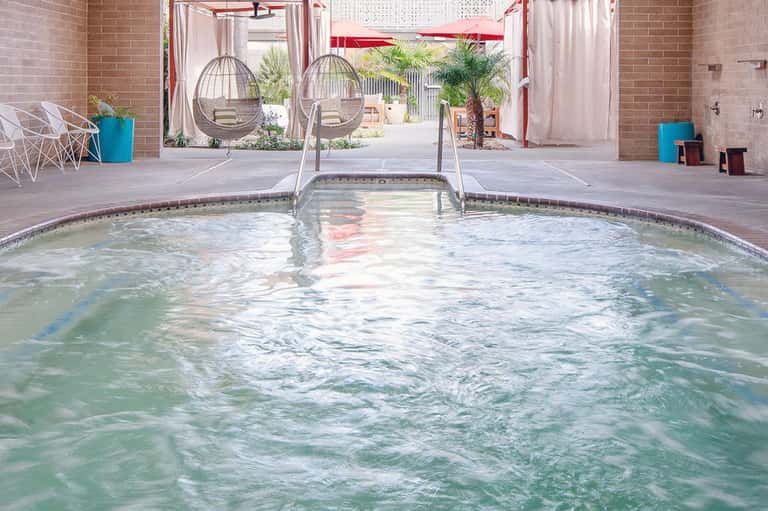 Indoor hot tub with water jets and hanging swing chairs in a brick courtyard with red umbrellas
