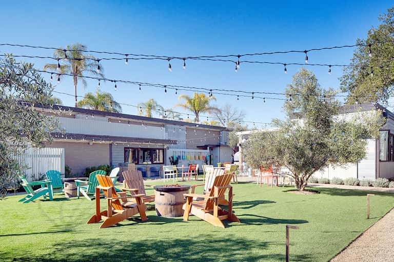 Outdoor lawn area with colorful Adirondack chairs arranged around a fire pit under string lights