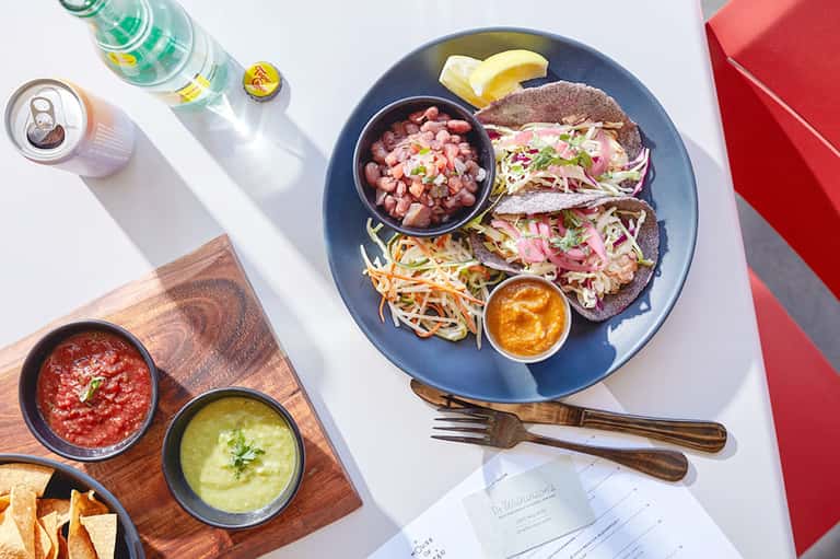 Plate of tacos with ceviche, salsa, and garnishes on blue plate with beverages