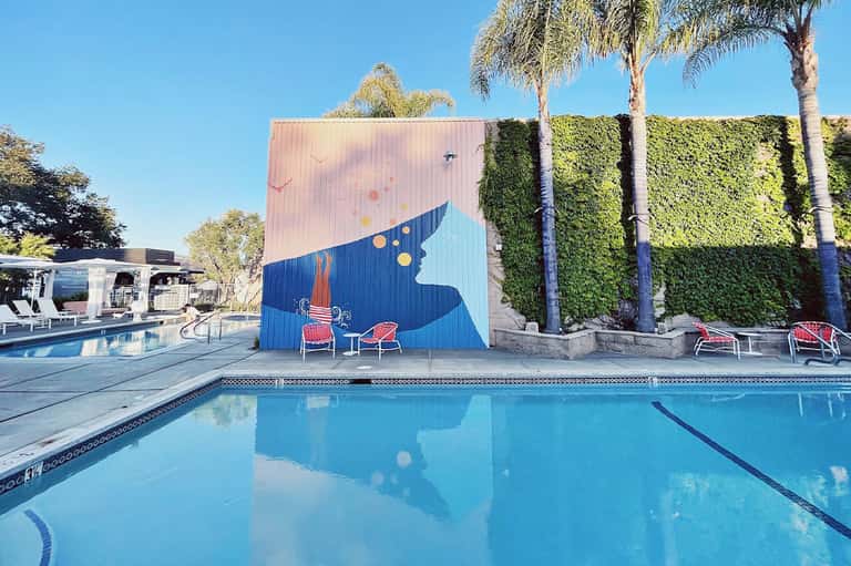 Resort pool with artistic mural wall, red lounge chairs, palm trees, and clear blue water