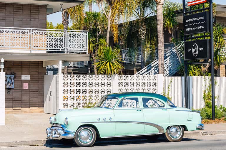 Vintage mint-green and blue 1950s Buick parked outside modern wellness resort building