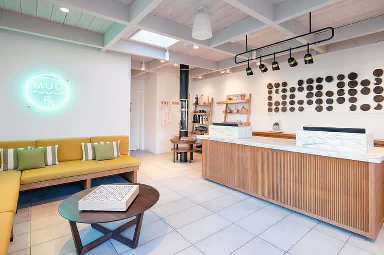 Modern spa reception area with yellow sofa, neon sign, and wooden counter