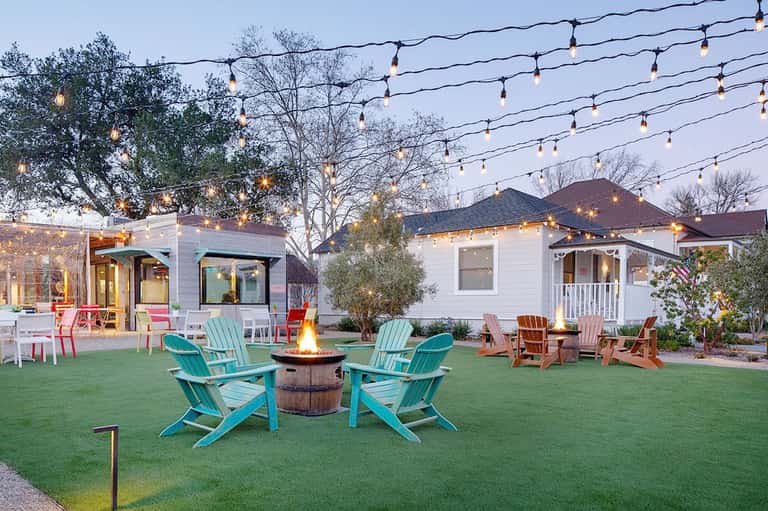 Backyard patio with firepit, turquoise Adirondack chairs, string lights, and modern white houses at dusk
