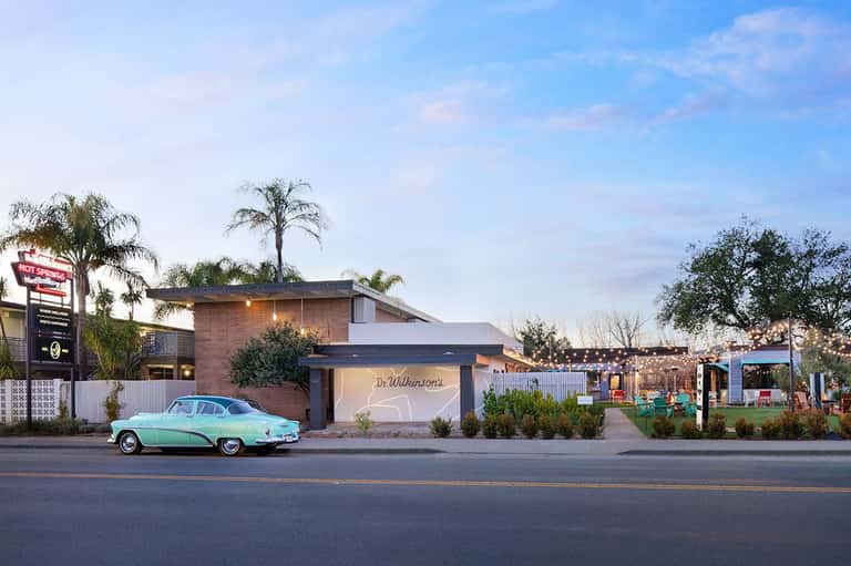 Retro-style hotel entrance with turquoise vintage car parked outside at dusk