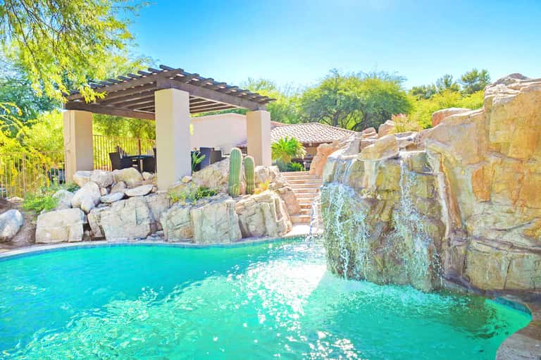 Luxury resort pool with turquoise water, rocky features, pergola, and desert landscaping