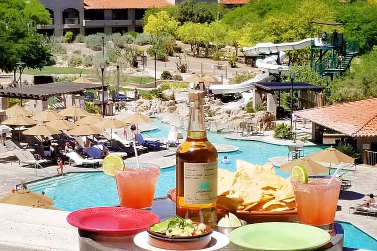 Colorful cocktails and appetizers on resort balcony overlooking pool and landscaped grounds