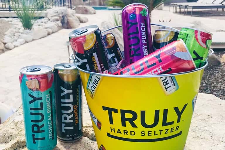 Colorful Truly Hard Seltzer beverage bucket on sandy beach with resort pool area