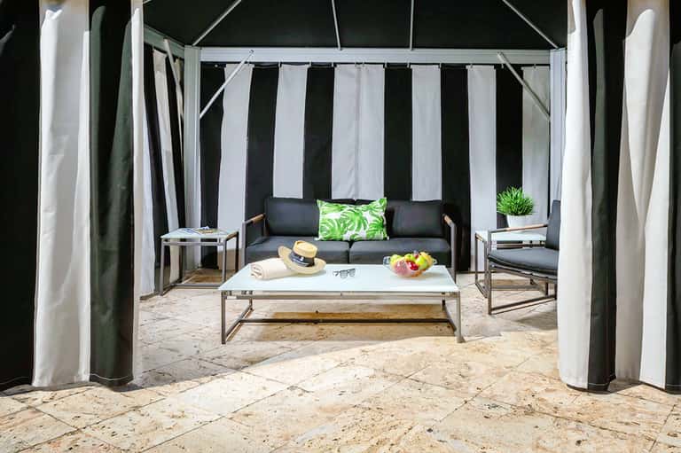 Private cabana on beach with black and white striped curtains, sofa, and white pillows