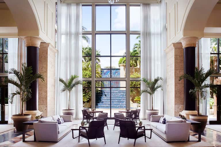 Luxurious resort lobby with towering columns, potted palms, sheer white curtains, and elegant seating areas