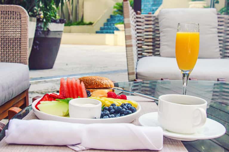 Outdoor dining table with fresh breakfast, fruit plate, sandwich, juice, and resort patio setting