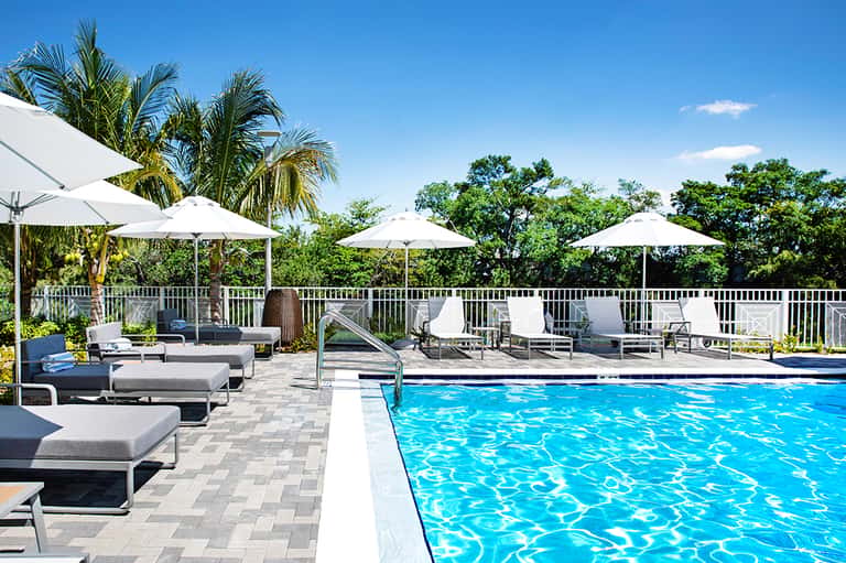 Modern resort pool with white umbrellas, lounge chairs, and lush tropical surroundings