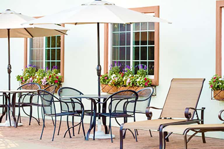 Beachfront patio with white umbrellas, lounge chairs, flowering planters, and ocean view